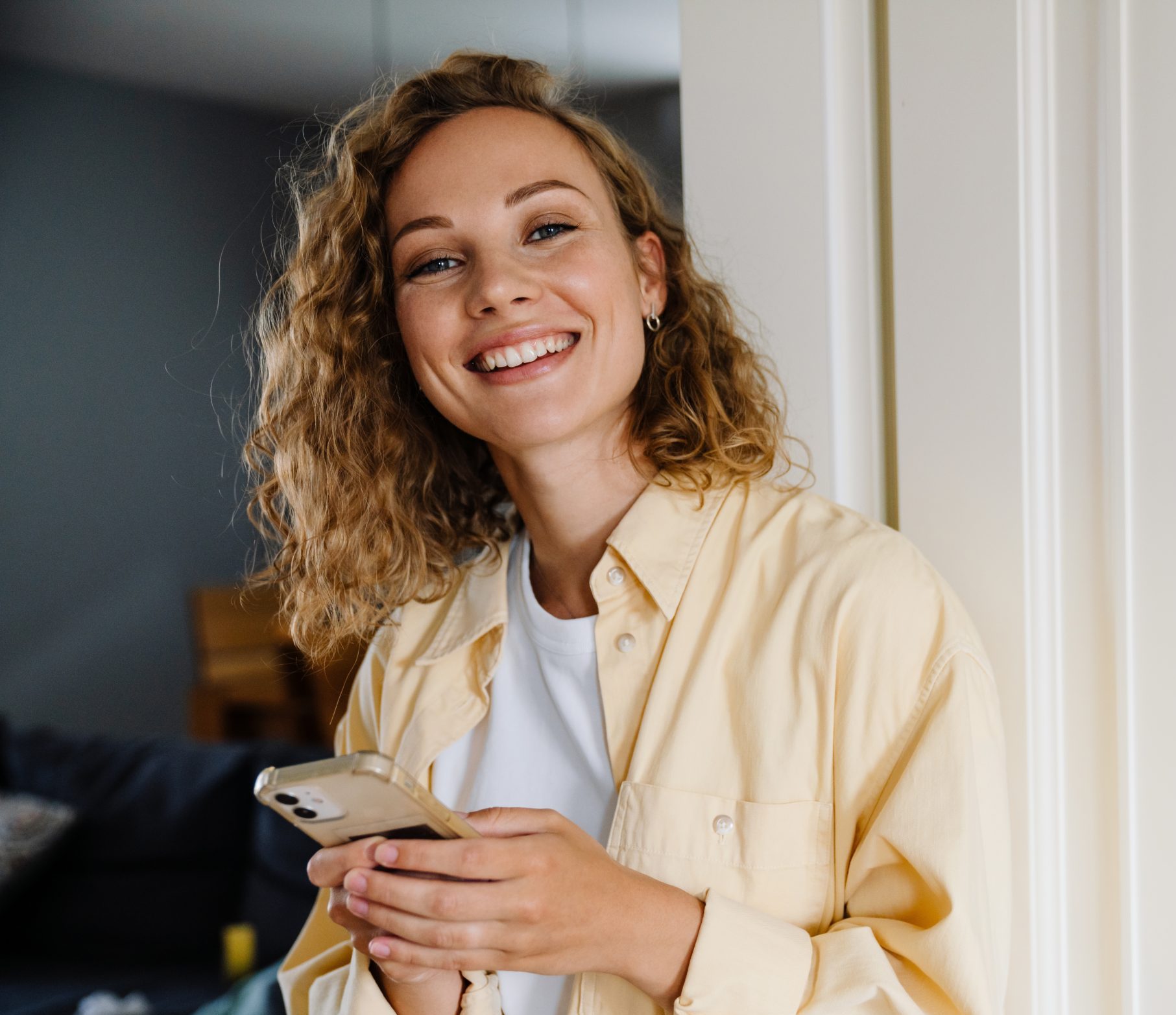 Smiling woman with curly hair holding a phone at home