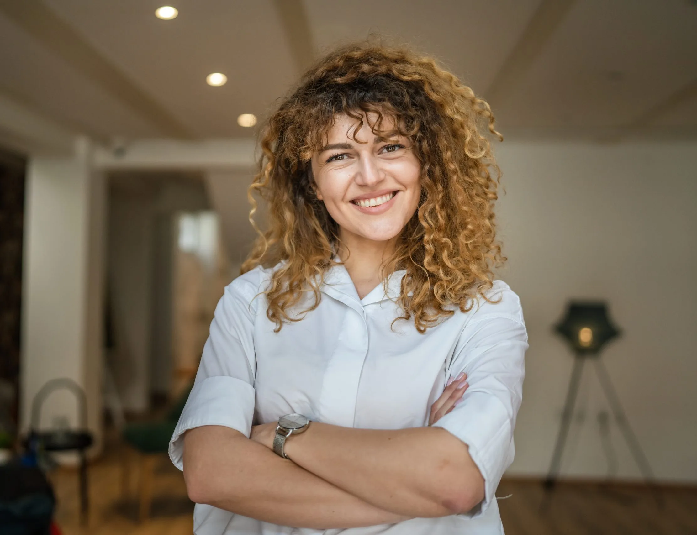Smiling woman with curly hair and arms crossed in a living room