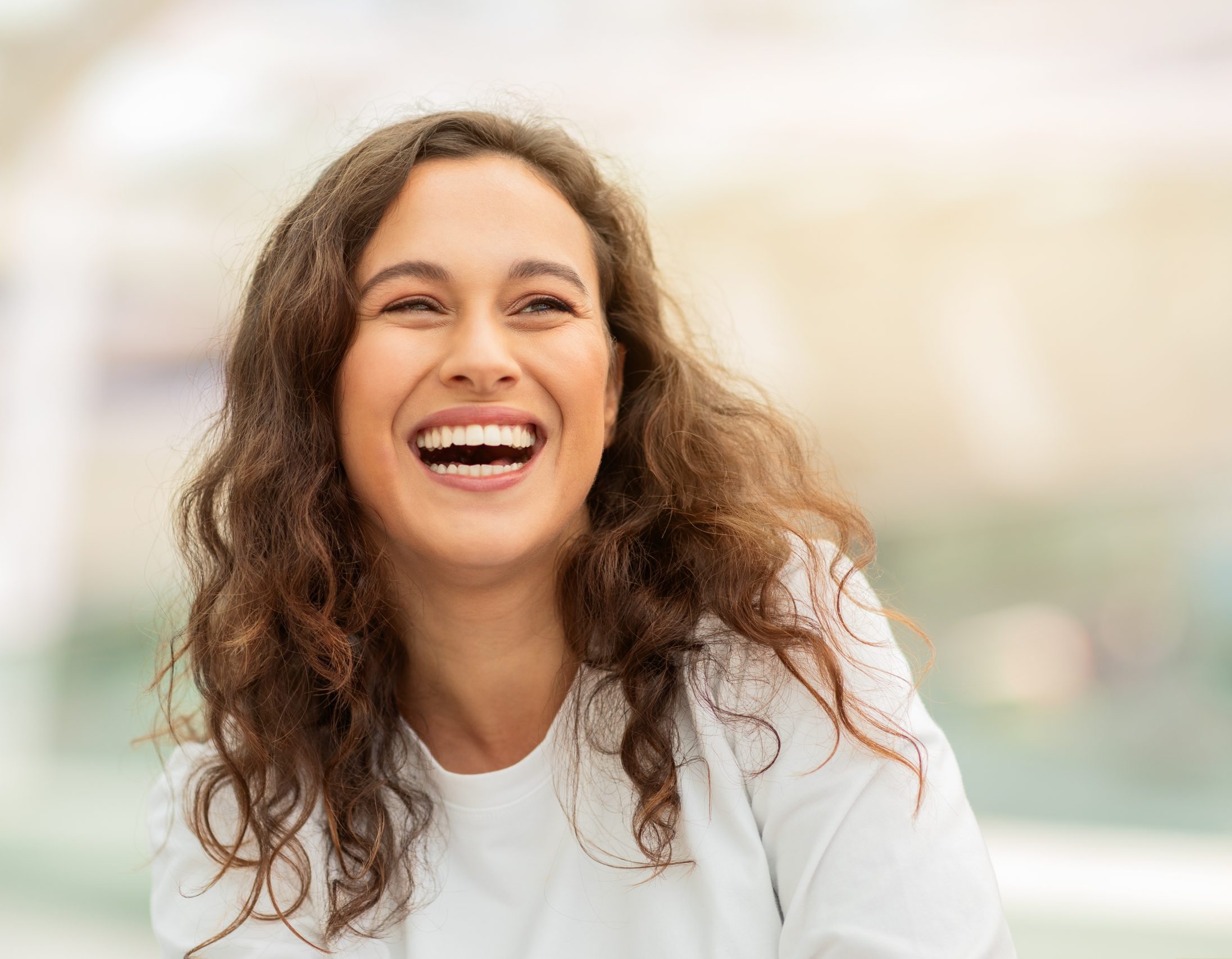 Laughing woman with curly hair outdoors in soft light