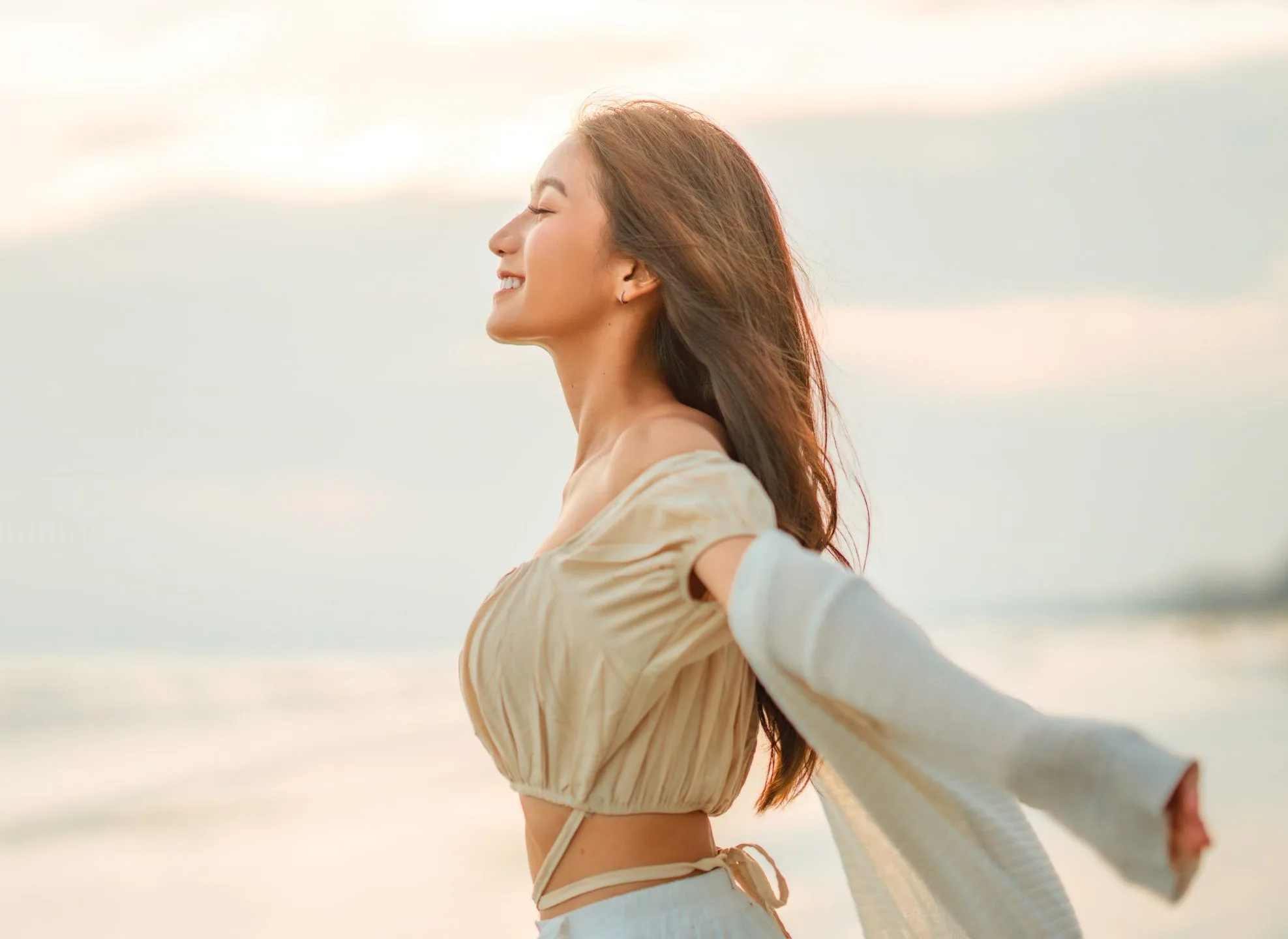 Woman with arms outstretched on a beach at sunset