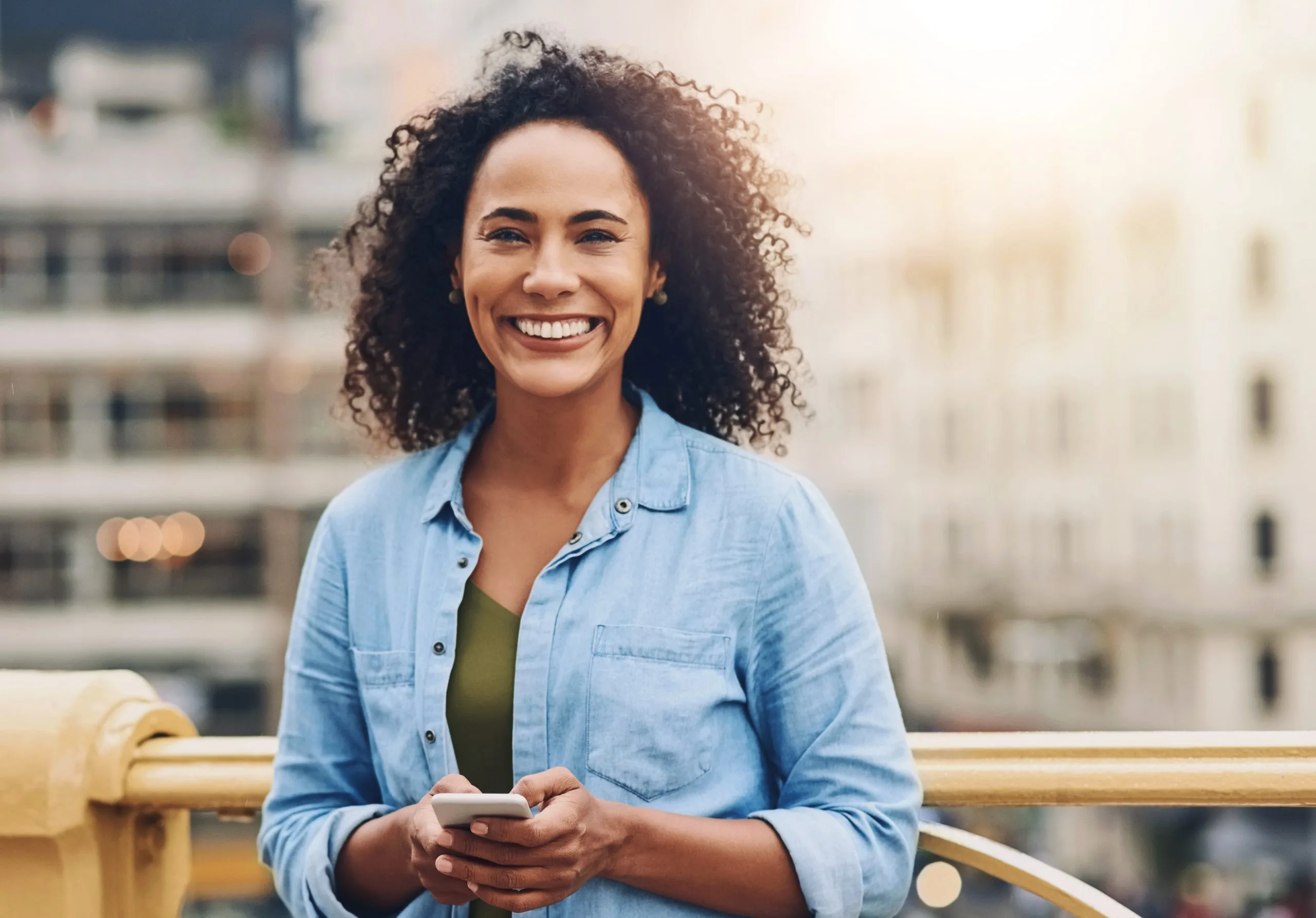 Smiling woman with curly hair on a city balcony
