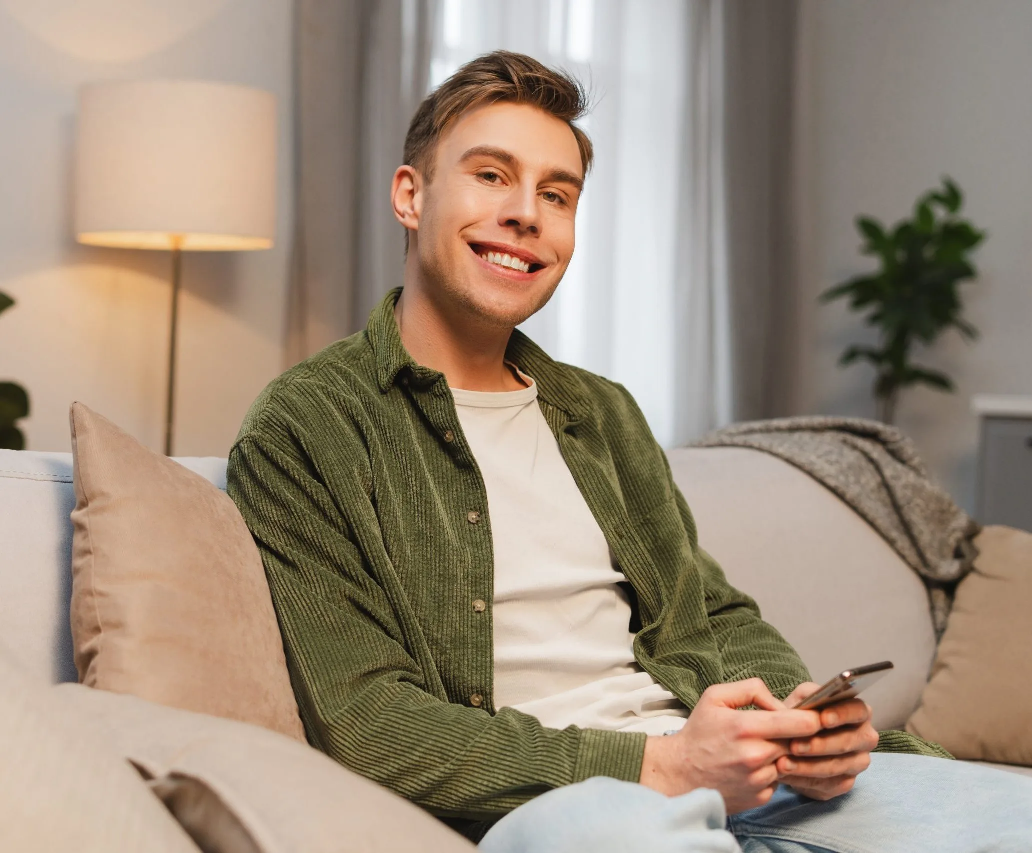 Smiling young man relaxing on a sofa with a phone