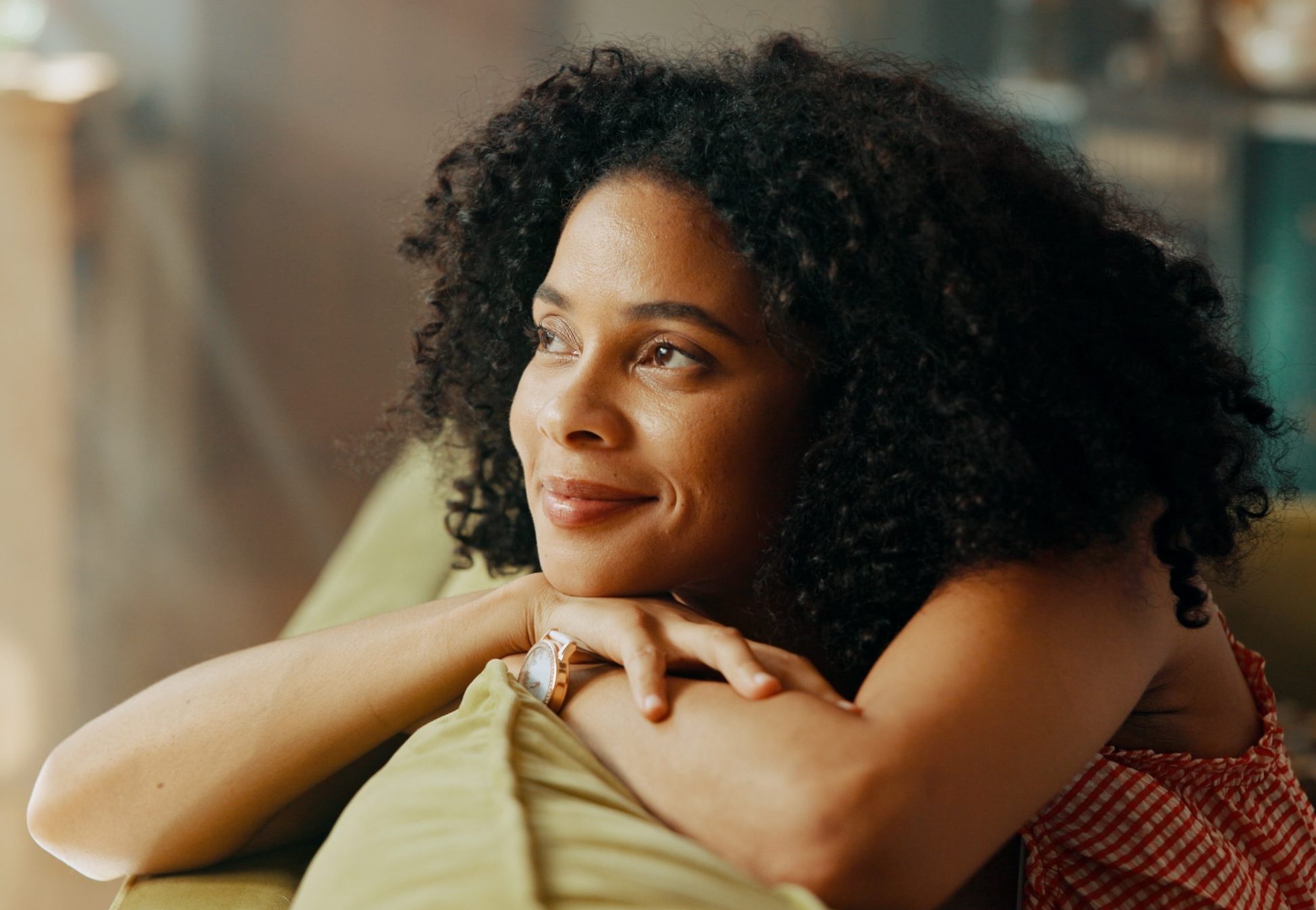 Woman with curly hair resting her chin on her hands at home
