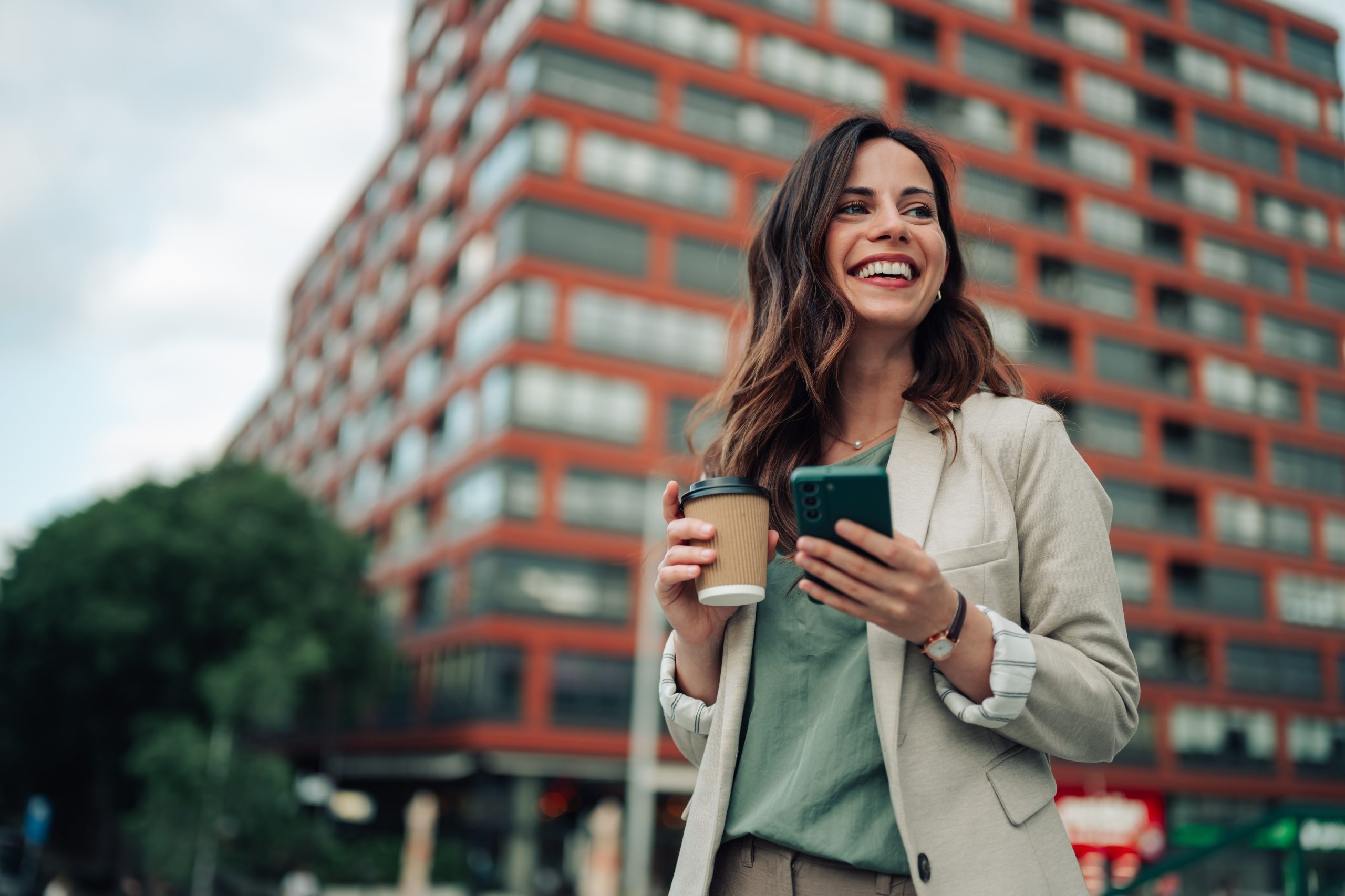 Smiling woman holding a phone on a city street