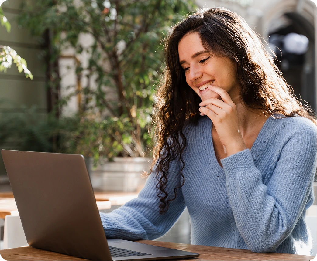 Woman smiling while using a laptop for a telehealth consultation in a bright, plant-filled space
